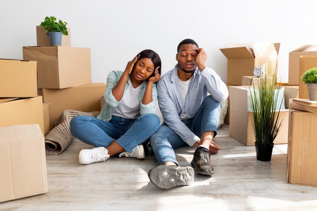 Couple Stressed On Moving Day Sat On Living Room Floor Surrounding By Carboard Boxes For Moving Out
