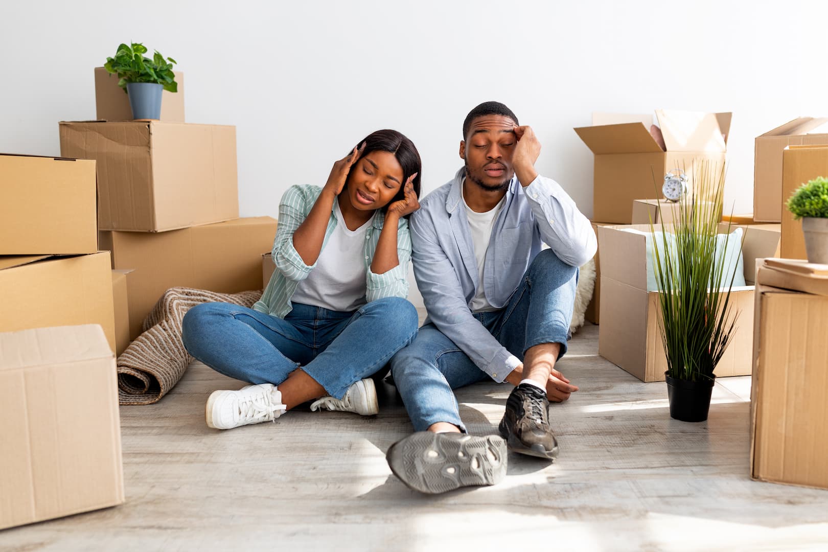 Couple Stressed On Moving Day Sat On Living Room Floor Surrounding By Carboard Boxes For Moving Out